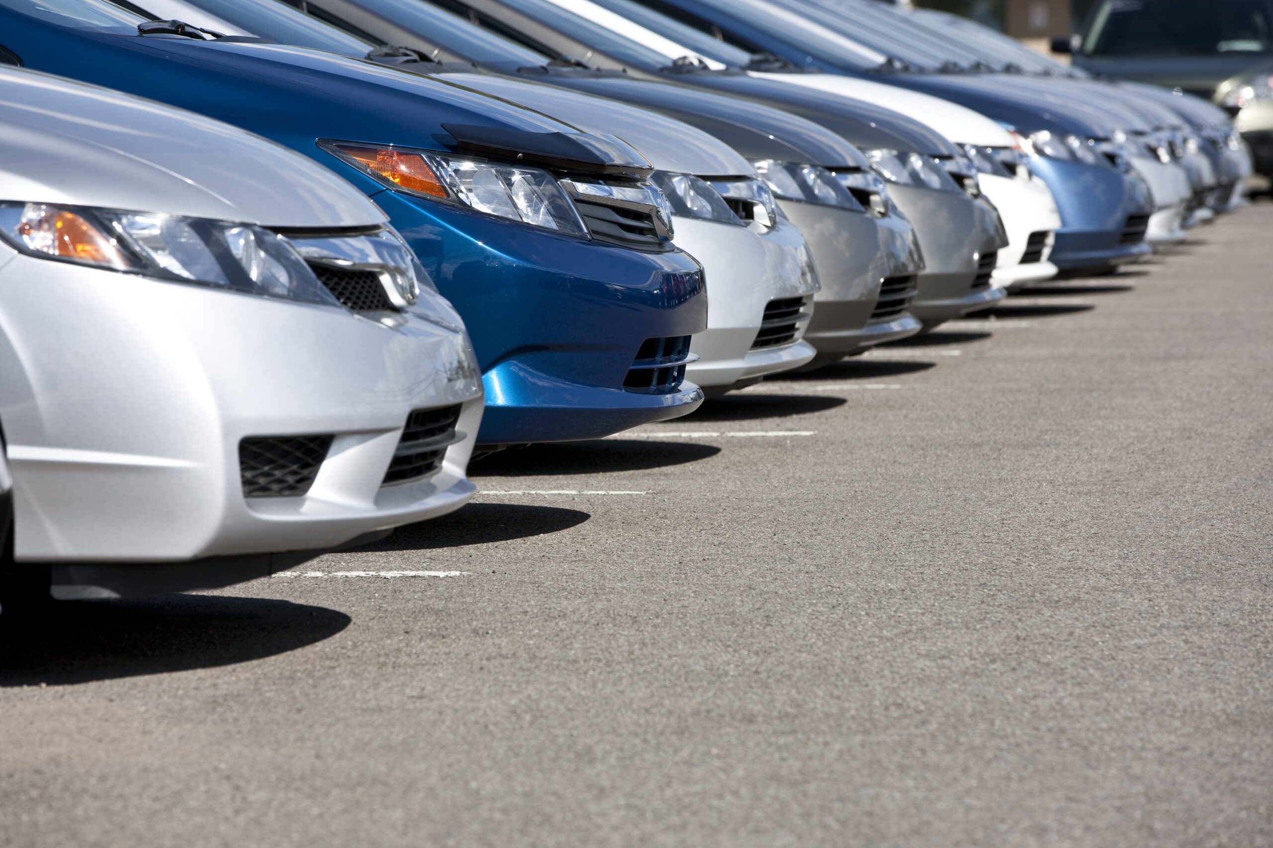 Lineup of new fuel efficient compact cars in dealership's parking lot, narrow depth of field.