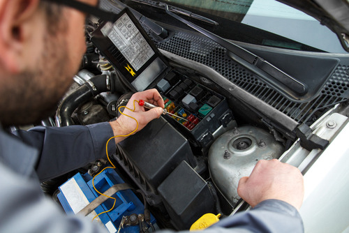 Mechanic diagnosing fuses under a hood.